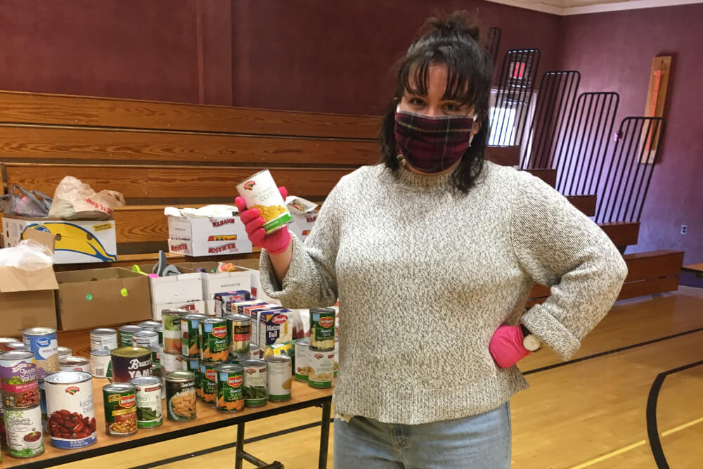 Woman wearing face mask holds canned food during a food drive