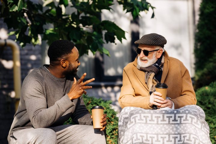 A younger man holds up three fingers while talking to an older man