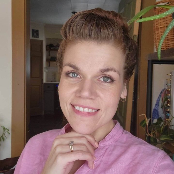 A woman smiles at the camera. She's wearing a pink shirt and her hair is up.