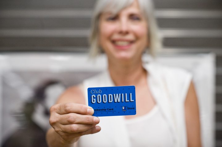 Woman smiling and holding a blue polka dotted Club Goodwill membership store card.