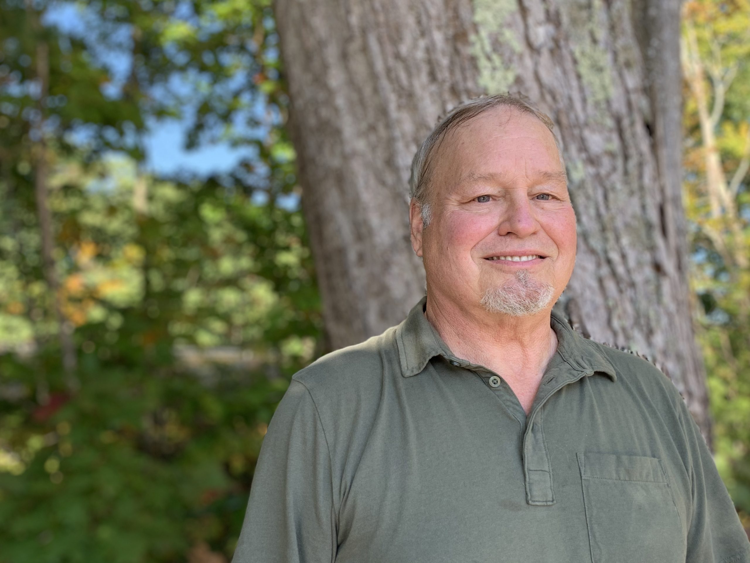 Man smiling with a green shirt with trees in the background. He is a staff member of Goodwill's LifeWorks Deaf Services