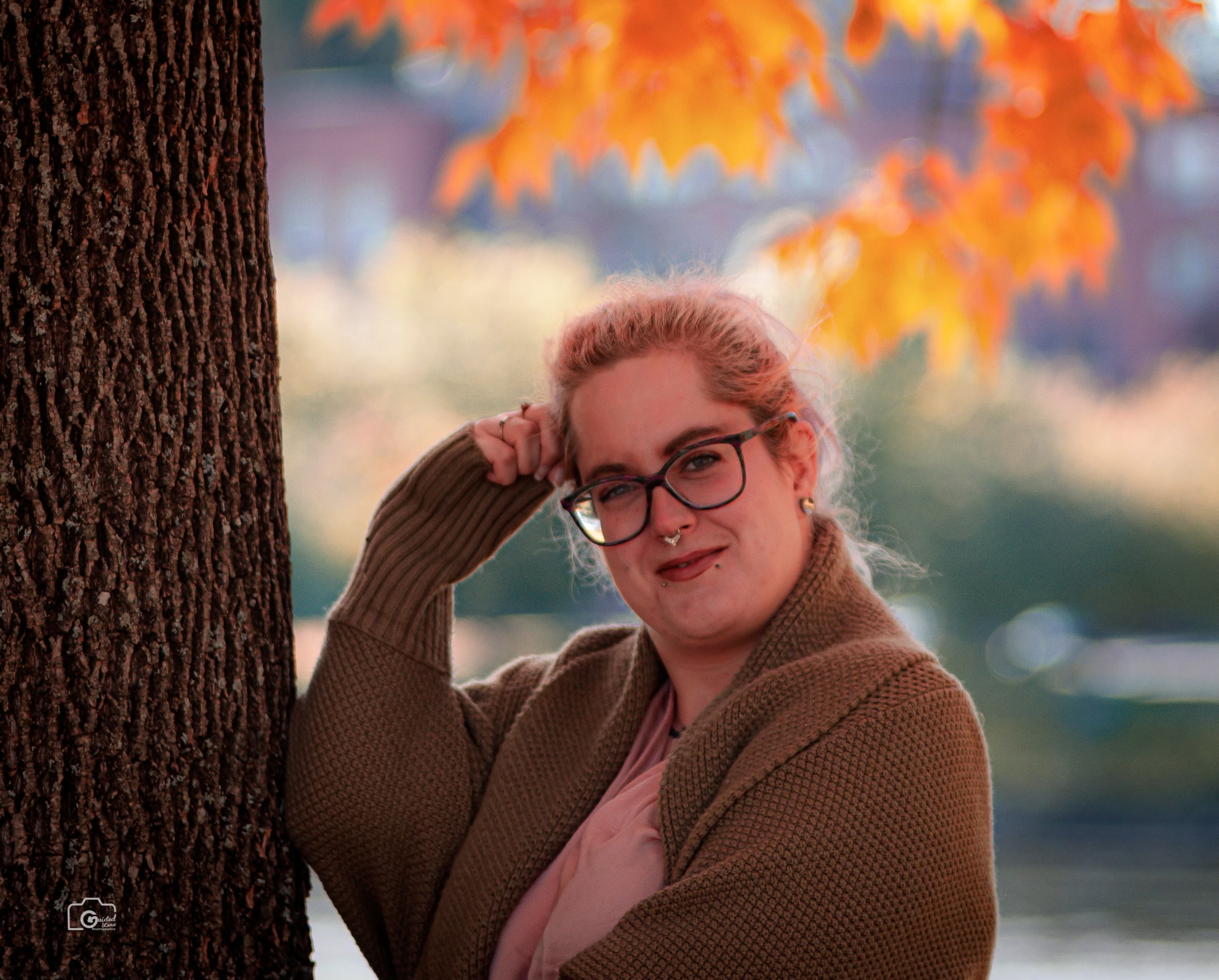 Successful career woman leaning against a tree smiling fall foliage in background