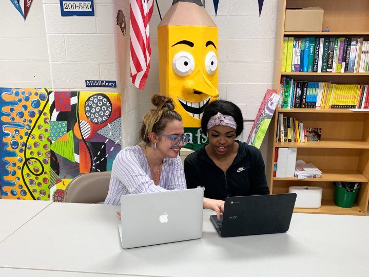 Megan Dalton sits with a student she is helping with college applications. Dalton is a member at the Aspirations Lab of Lewiston High School. In the photo a woman sits next to a young woman at a table, they each have laptops in front of them and they're smiling while looking at the computers.