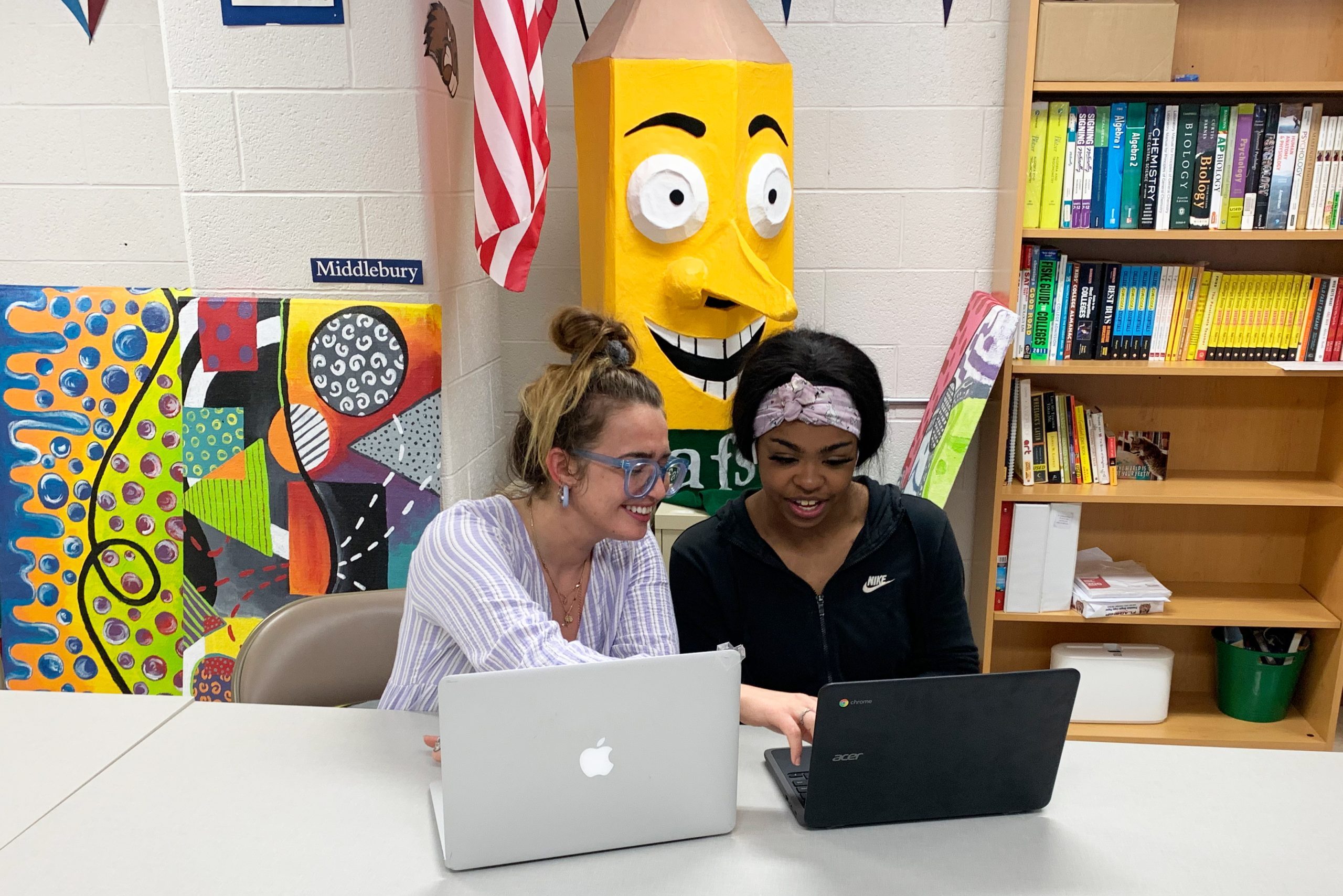 Megan Dalton sits with a student she is helping with college applications. Dalton is a member at the Aspirations Lab of Lewiston High School. In the photo a woman sits next to a young woman at a table, they each have laptops in front of them and they're smiling while looking at the computers.