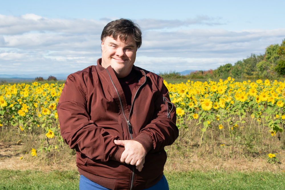 Man stands smiling in front of a sunflower field