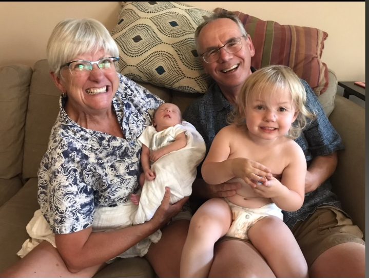 Man and woman holding their two grandchildren. One grandchild is an infant and the other is a toddler. 