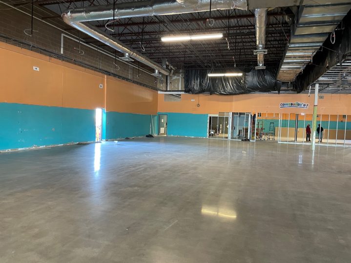 A large, empty room with no ceiling, very shiny waxed floors and a blue and orange painted wall.