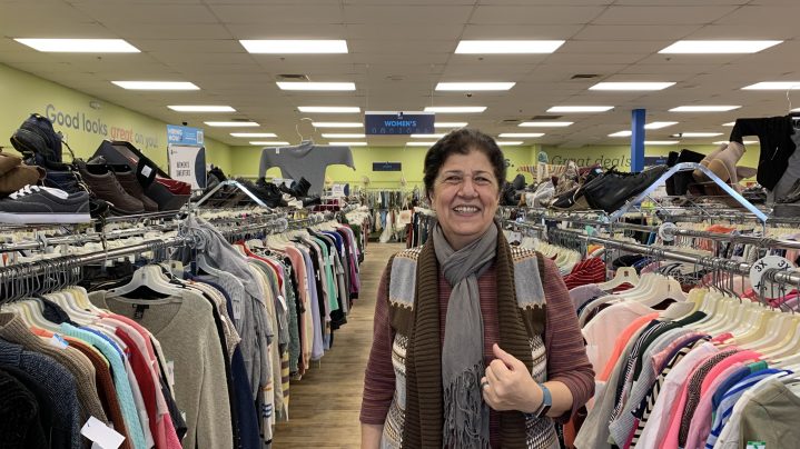 Rajaa Allahan, at her job at the Mill Creek Goodwill store, stands between  two racks of clothing. 