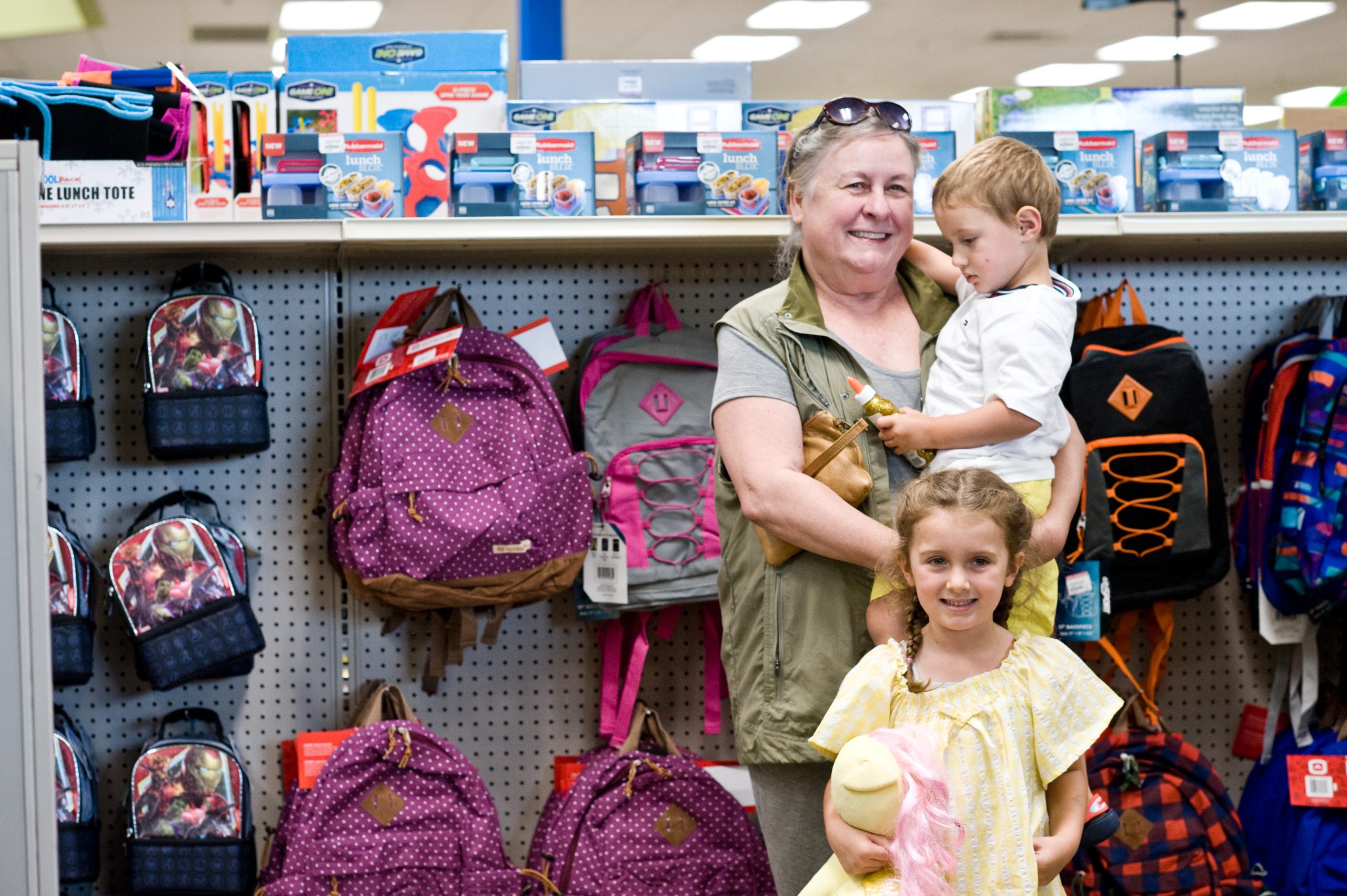 A woman stands with two young children in the backpack aisle at their local Goodwill retail store.