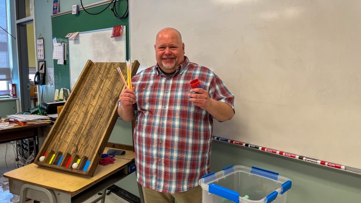 Richard Alley, career advisor, wears a plaid shirt and is in front of the classroom with teaching items. He is smiiing at the camera. 