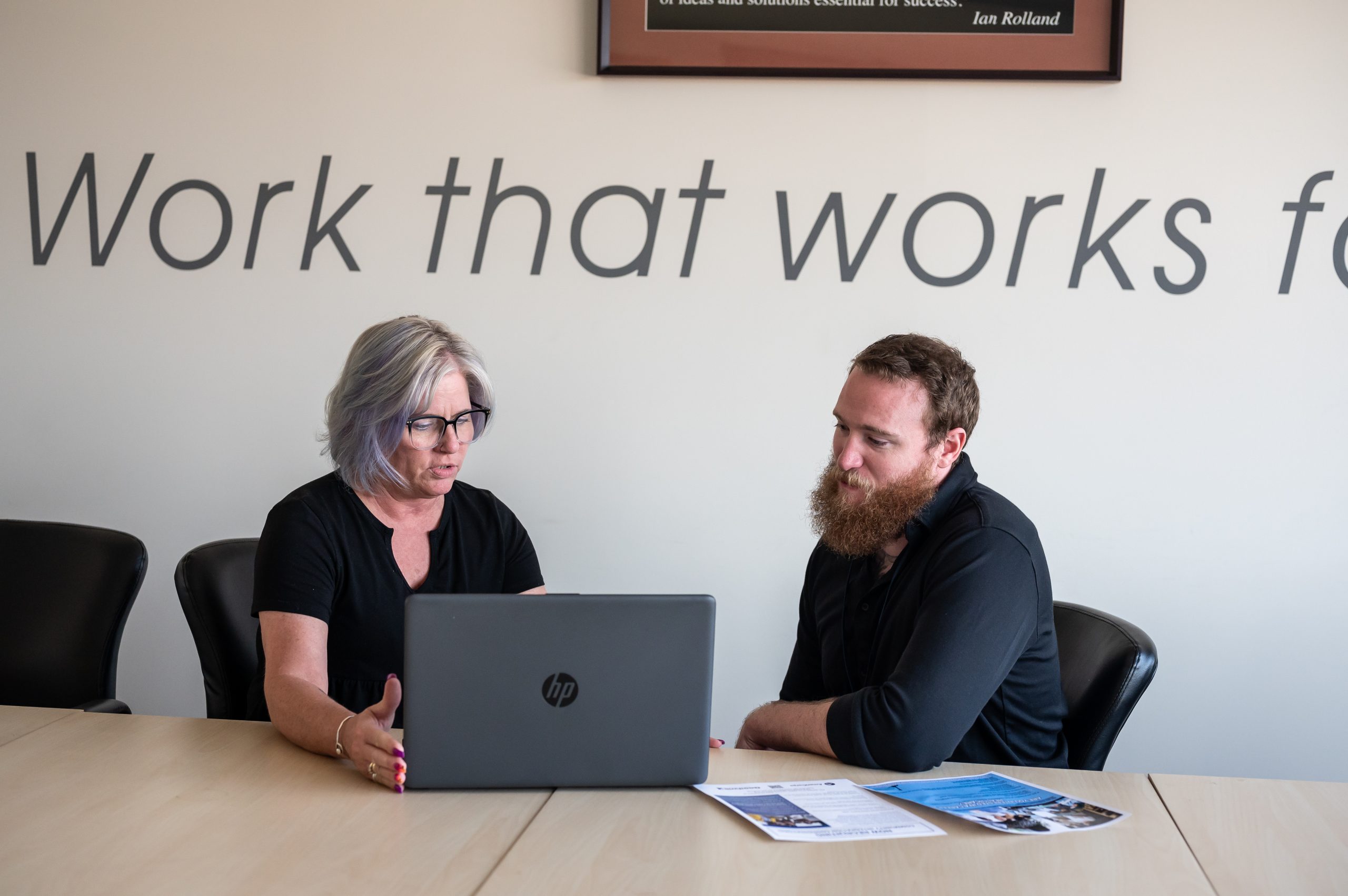 A woman and man sit at a table looking at a laptop.