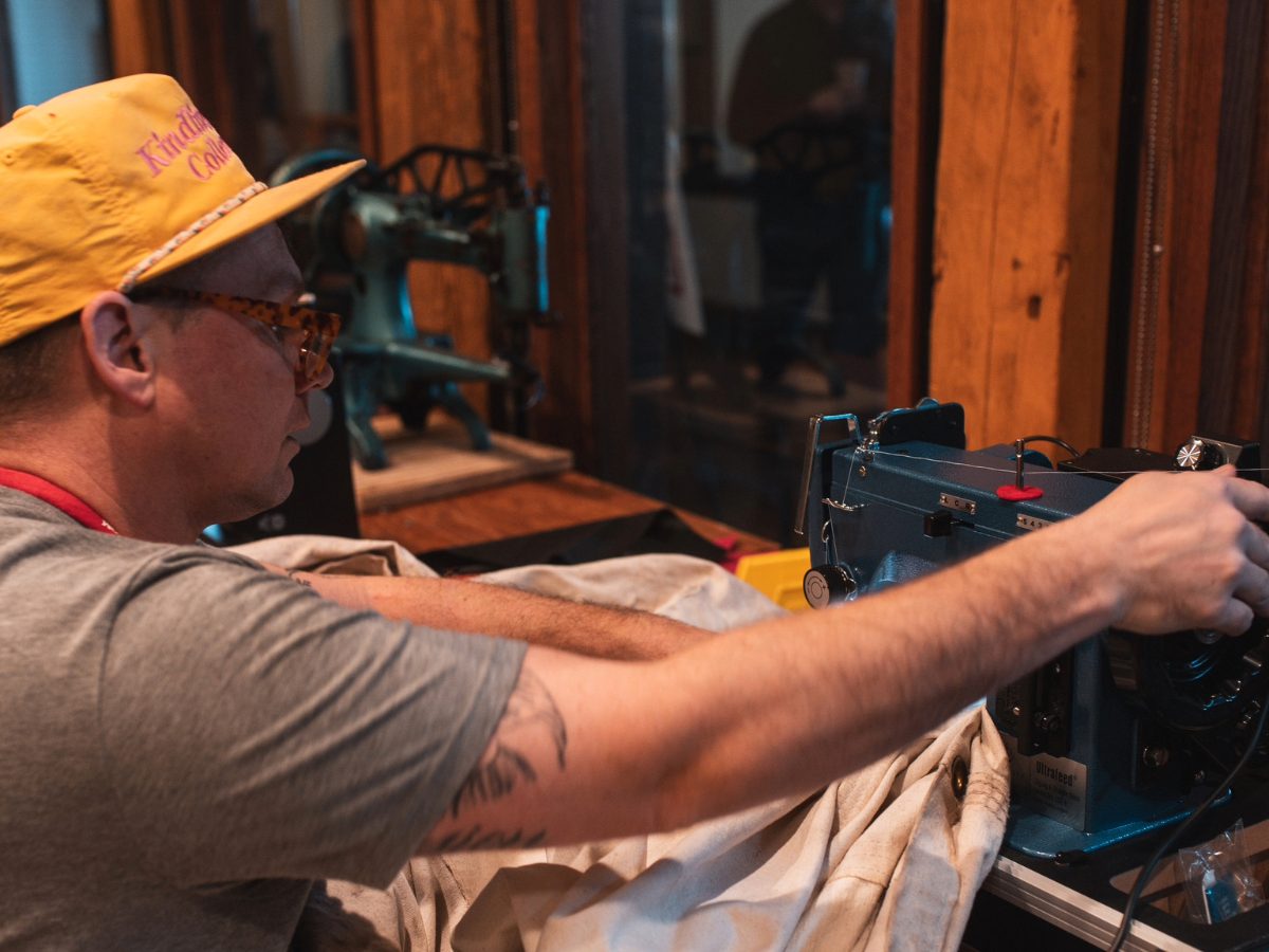 man wearing a yellow hat sitting at a sewing machine and repairing a jacket