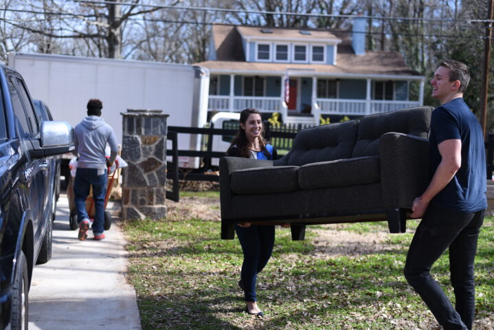 A woman and a man carrying a donated couch outside.