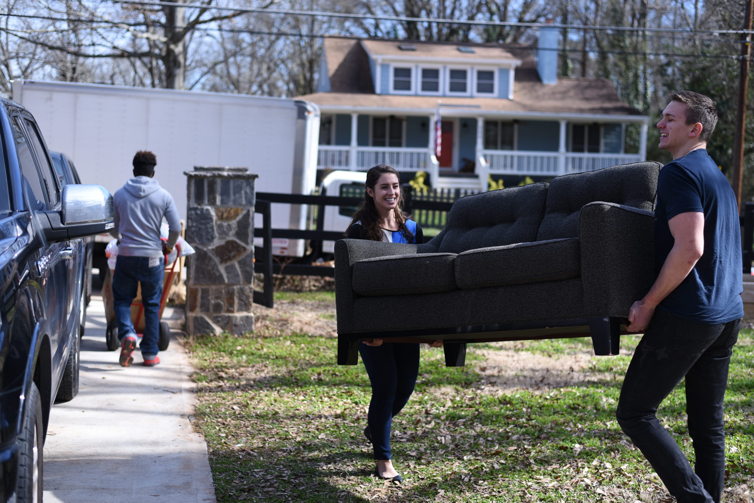 A man and woman carrying a couch outside.