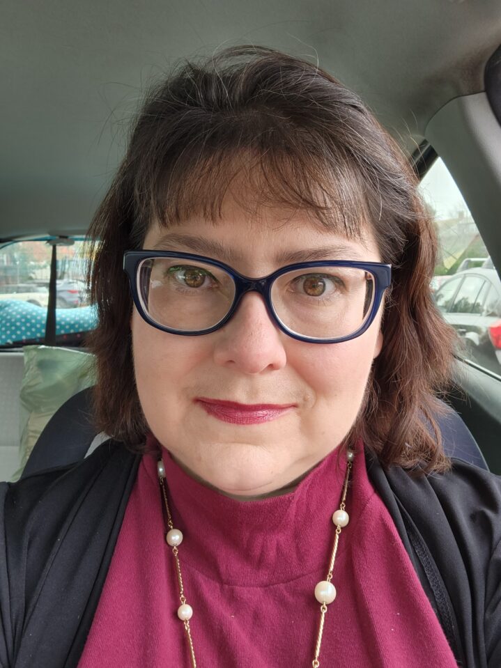 A smiling woman, Stephanie, wearing glasses and lipstick.