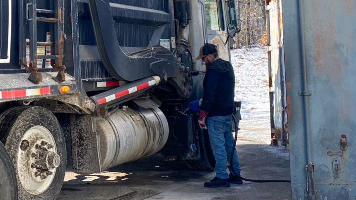 A man fueling up a garbage truck.