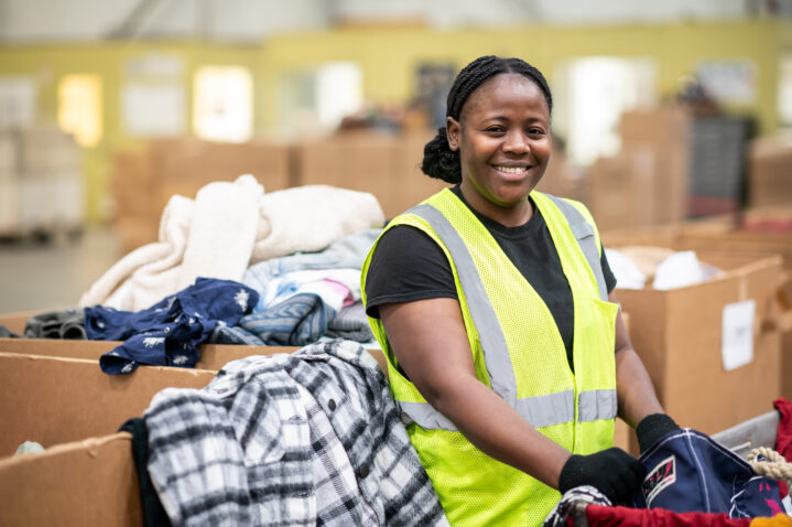 A woman wearing a yellow safety vest smiling and leaning against a big box of stuff.