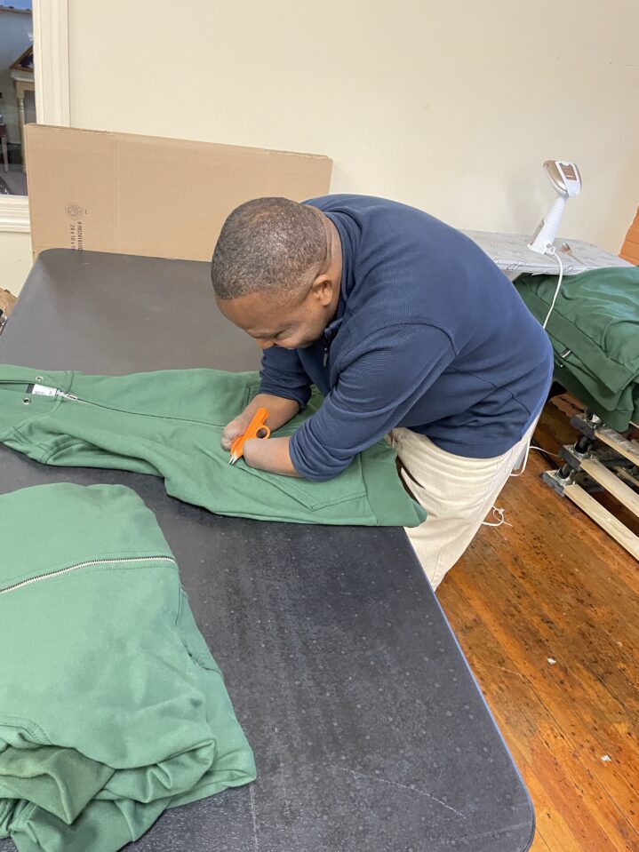 A man with no hands working on a uniform with a tool.